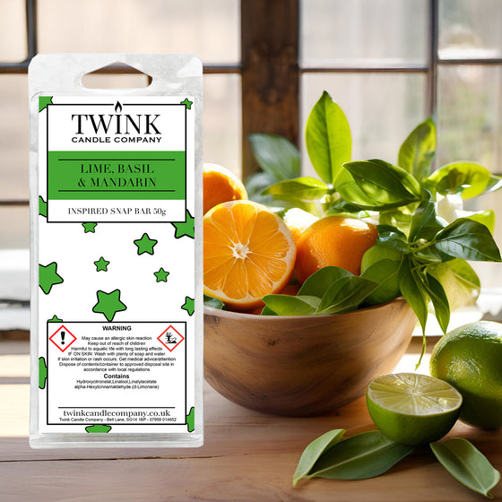 Lime, Basil & Mandarin soy wax melt snap bar by Twink Candle Company, beside a wooden bowl of limes, mandarins and fresh basil