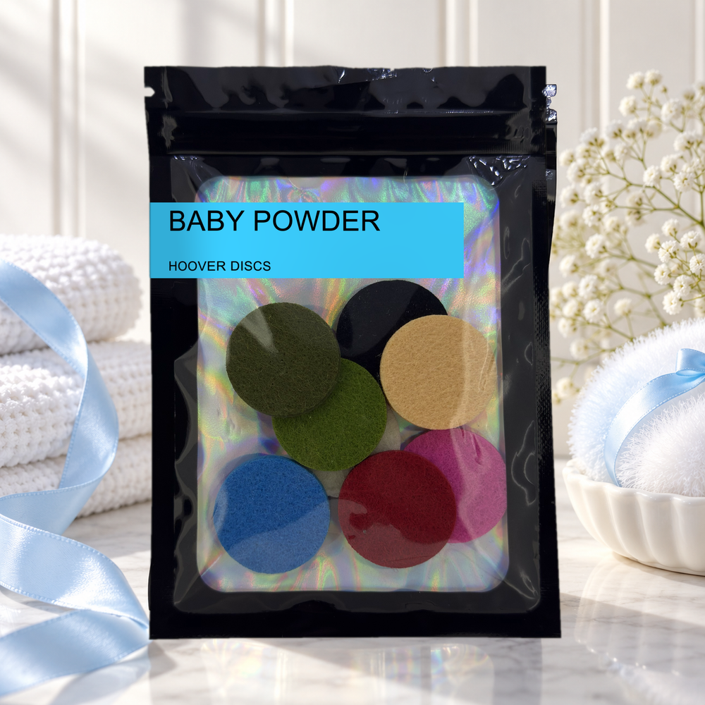 Pack of 8 Baby Powder scented hoover discs in its sealed black foil packet beside folded white towels, blue ribbon and gypsophila