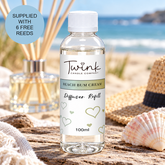 Beach Bum Cream reed diffuser refill by Twink Candle Company, a 100ml bottle on driftwood on a sunlit beach with a straw hat and shell