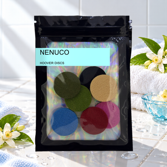 Pack of 8 Nenuco scented hoover discs in its sealed black foil packet beside white towels, orange blossom and a blue glass dish