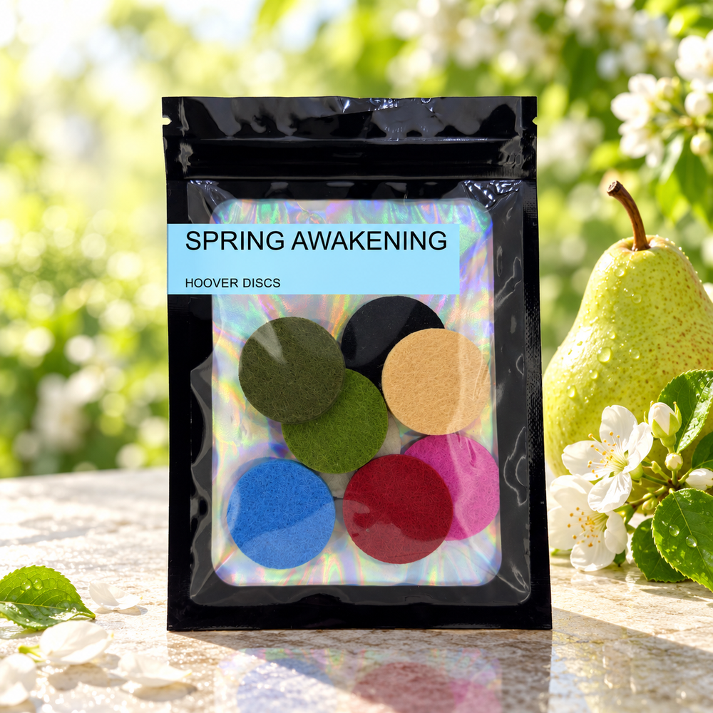 Pack of 8 Spring Awakening scented hoover discs in its sealed black foil packet beside a green pear and white blossom