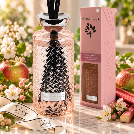 Woodbridge Summer Breeze 1000ml reed diffuser in a pink woven glass bottle with black reeds on pale marble, beside its pink gift box with apple blossom, apples and rhubarb, and a Twink Candle Company ribbon