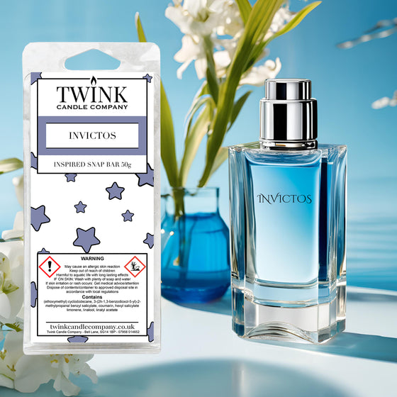 Invictos inspired soy wax melt snap bar by Twink Candle Company, beside a blue glass perfume bottle and white flowers