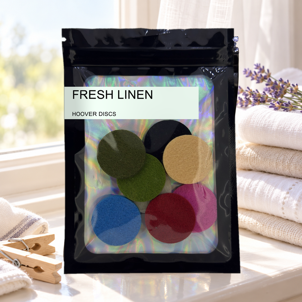 Pack of 8 Fresh Linen scented hoover discs in its sealed black foil packet beside folded linens, lavender and wooden pegs