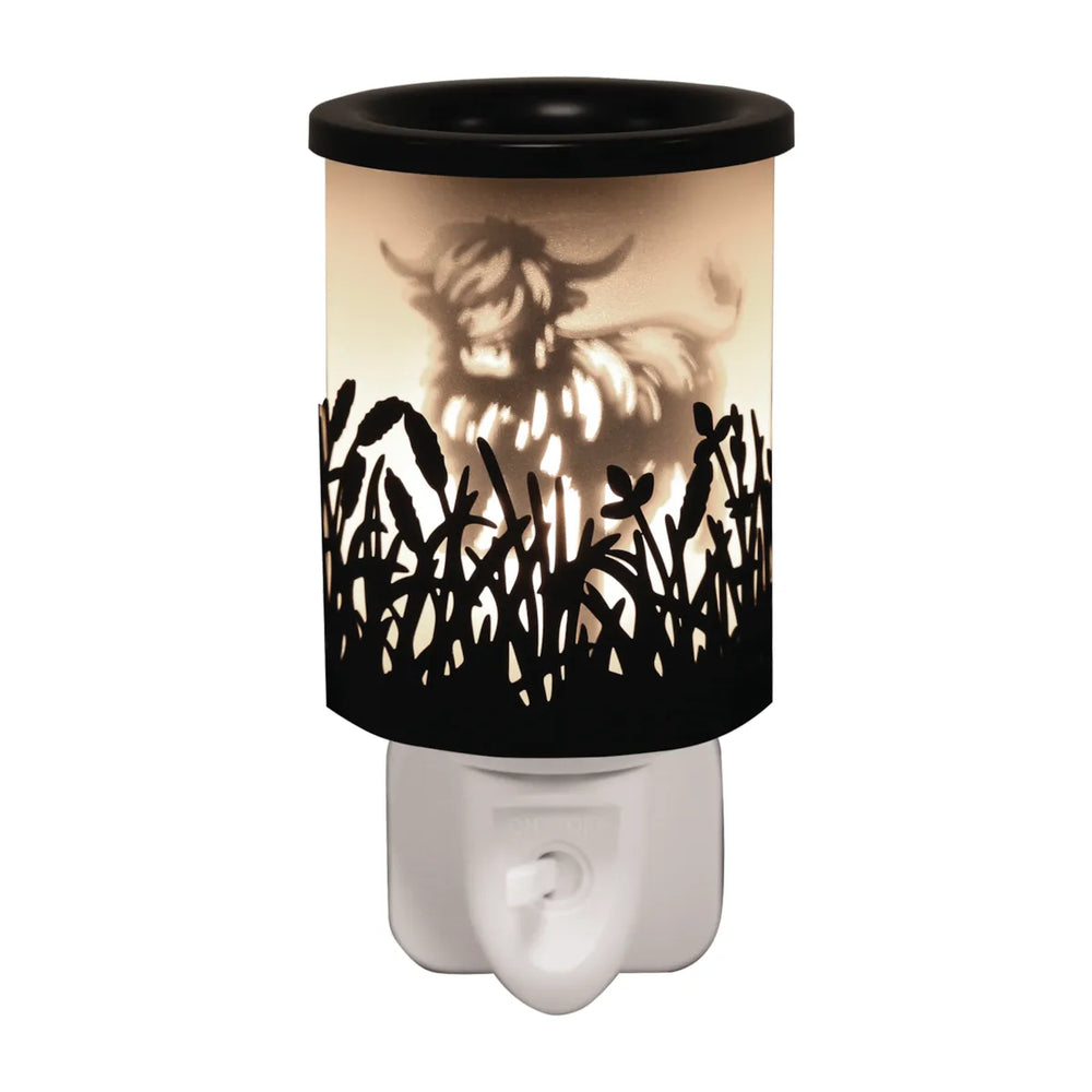 Highland Cow Black Shadow plug-in wax melt burner glowing warm, showing a highland cow silhouette among wildflowers