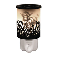 Highland Cow Black Shadow plug-in wax melt burner glowing warm, showing a highland cow silhouette among wildflowers