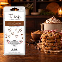 Santas Cookies inspired soy wax melt snap bar by Twink Candle Company, stood on a dark wood table beside a stack of chocolate chip cookies and a mug of hot chocolate