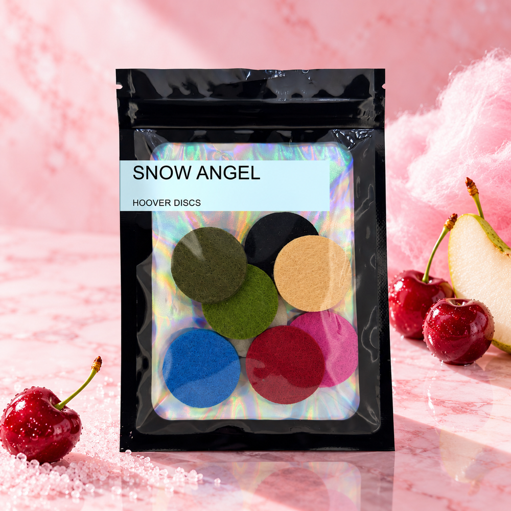 Pack of 8 Snow Angel scented hoover discs in its sealed black foil packet beside cherries, a pear slice and candy floss