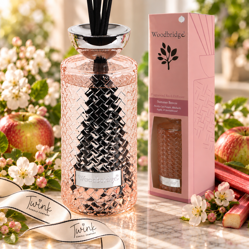 Woodbridge Summer Breeze 1000ml reed diffuser in a pink woven glass bottle with black reeds on pale marble, beside its pink gift box with apple blossom, apples and rhubarb, and a Twink Candle Company ribbon