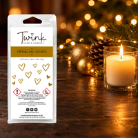 Twinkling Lights inspired soy wax melt snap bar by Twink Candle Company, stood on a dark wood table beside a lit candle, gold baubles and a pine cone
