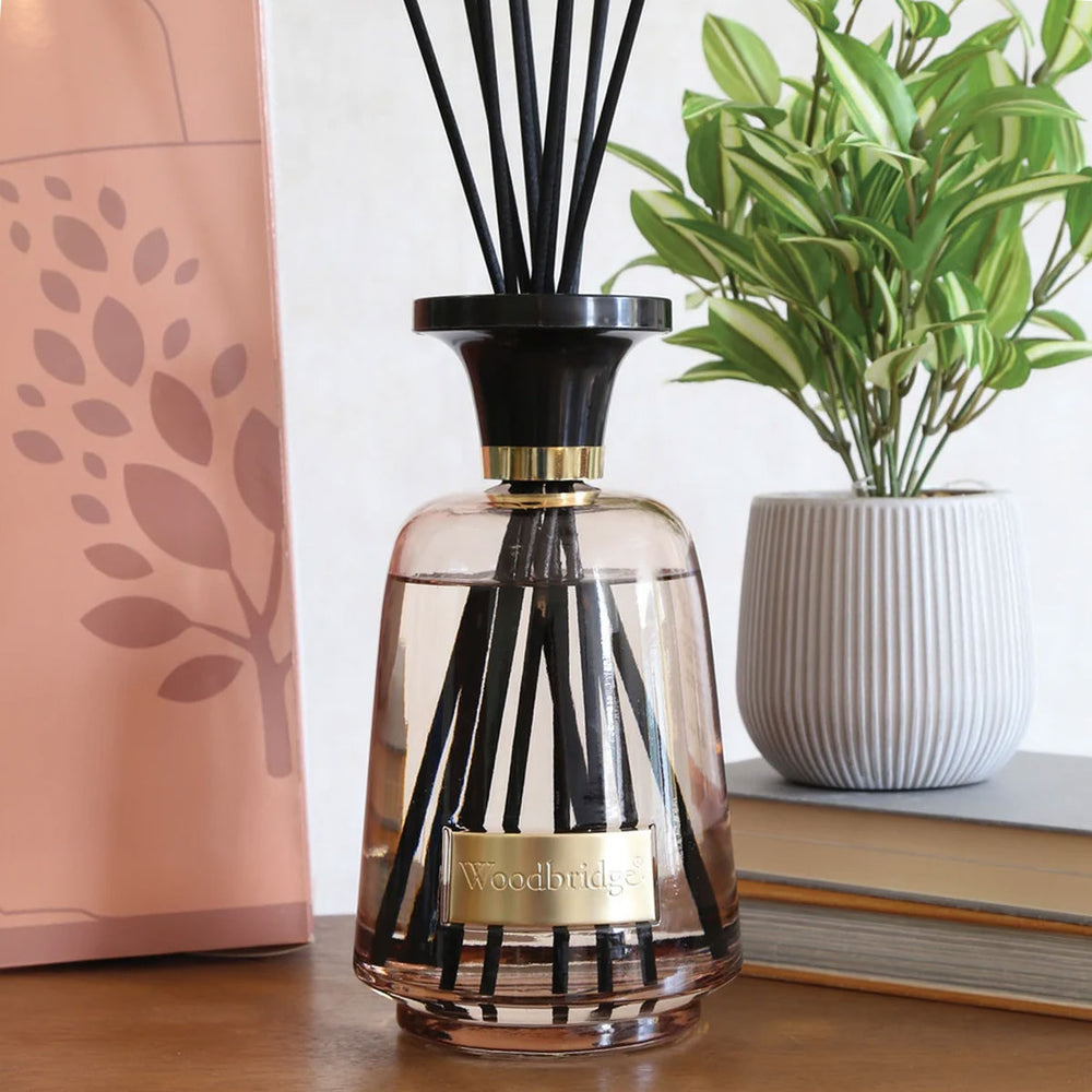 Woodbridge Oud Wood 1000ml reed diffuser — amber glass bottle with rattan reeds, styled in a warm home setting
