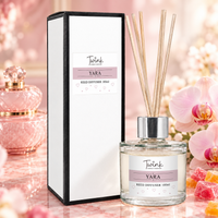 Yara reed diffuser by Twink Candle Company, a 100ml glass bottle with reeds beside its white gift box, on a blush pink marble surface with stacked pink perfume pots, orchid and candied fruit